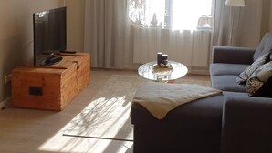 A living room with a sofa, a television on a wooden cabinet, a round glass coffee table, and a lamp.