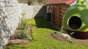 A fenced garden area with a wooden structure, a green bird feeder, and a stone wall.