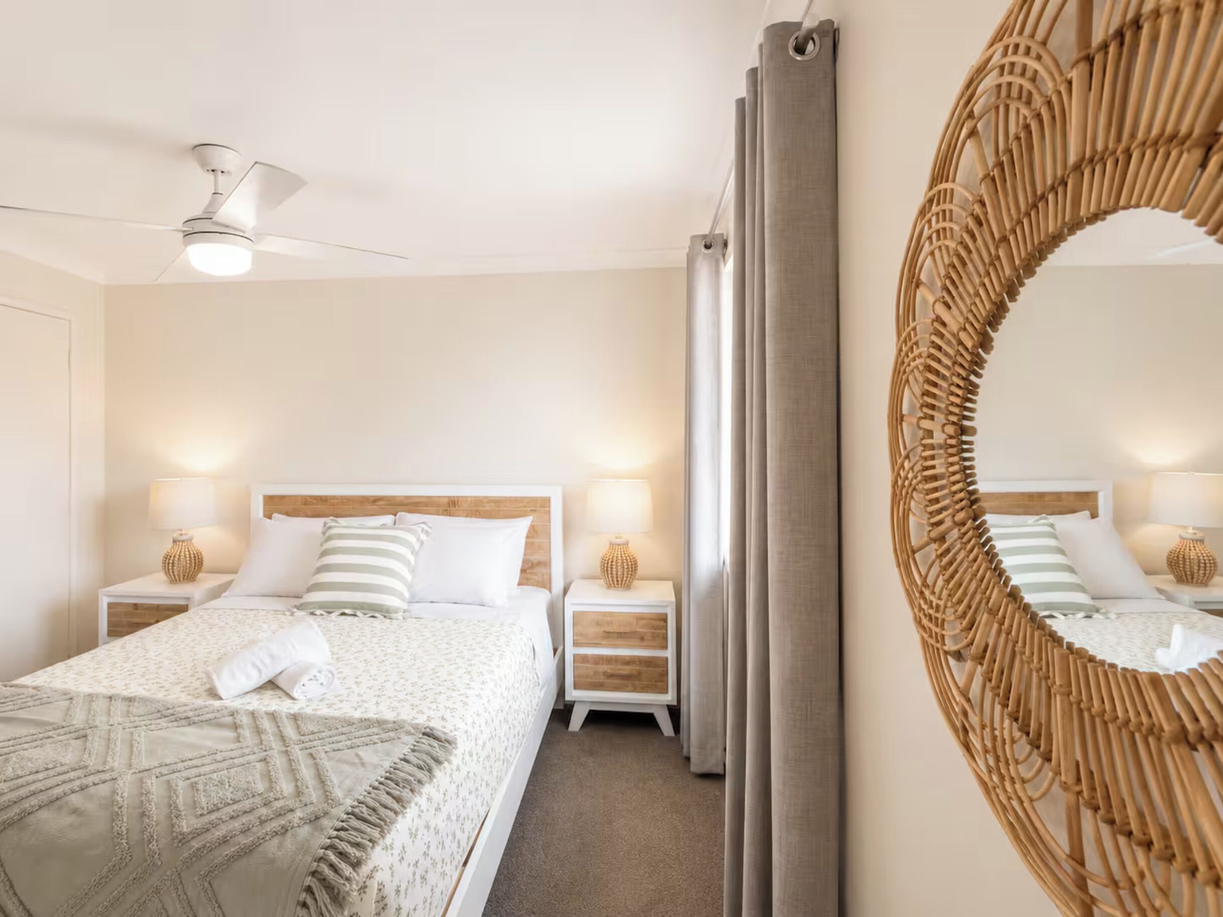 Un dormitorio con cama, dos mesitas de noche, un espejo en la pared y un ventilador de techo.