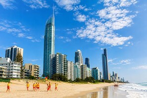 A beach with people, a sandy shore, and a city skyline with tall buildings. - Broadwater Paradise – Canal Views & Beaches (Runaway Bay)