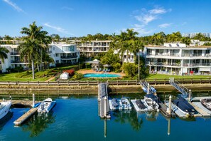 A marina with boats docked, a swimming pool, and multi-story buildings with balconies. - Broadwater Paradise – Canal Views & Beaches (Runaway Bay)