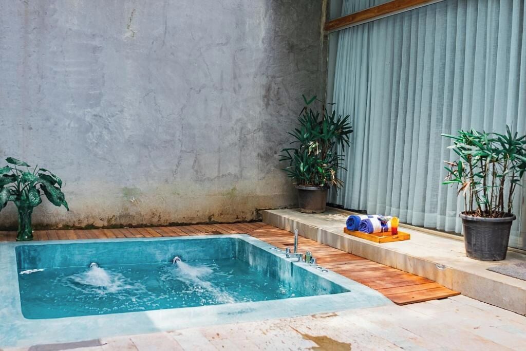 Ein rechteckiges Whirlpool mit Wasserdüsen, umgeben von einer Holzterrasse und Blumentöpfen.
