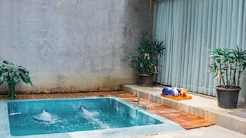 Ein rechteckiges Whirlpool mit Wasserdüsen, umgeben von einer Holzterrasse und Blumentöpfen.