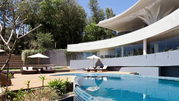 Uma área moderna à beira da piscina, com um edifício curvo, espreguiçadeiras e uma piscina azul límpida.
