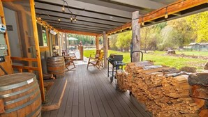 Un espacio al aire libre techado con mobiliario de madera, una parrilla y leña apilada.