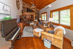 A cozy living room with a grand piano, leather sofas, a dining area, and a large window with blinds.