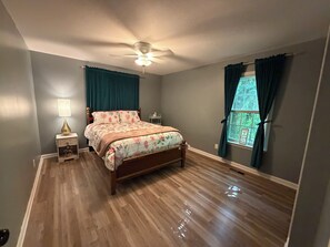 A bedroom with a wooden bed, a ceiling fan, a nightstand with a lamp, and a window with curtains. - 3-bed/1-bath Home in charming Pegram - TriStar Tribe Country Cottage (Pegram)