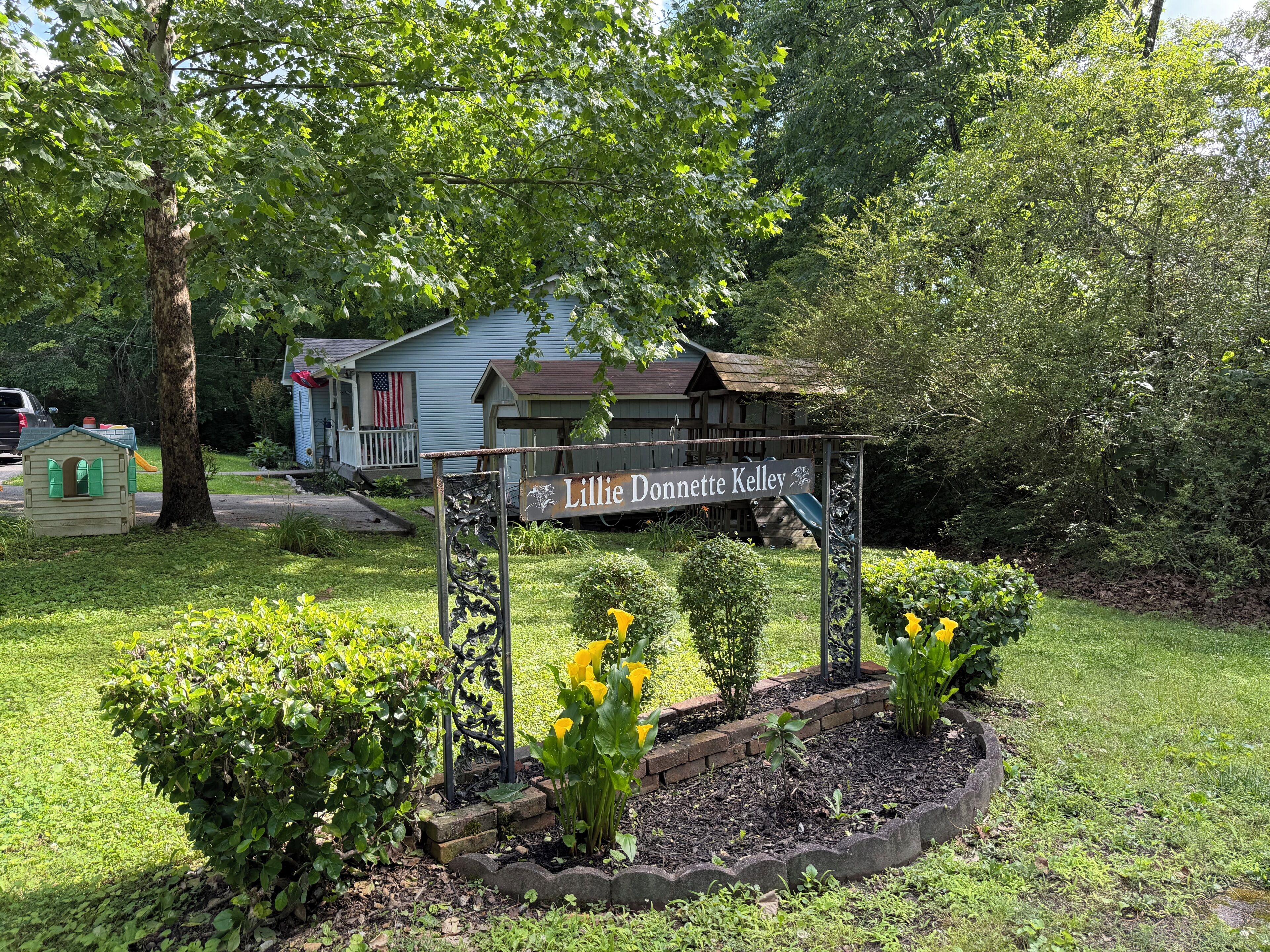 A sign with the name 'Lillie Donnett Kelley' in a garden area with a house in the background.. 3-bed/1-bath Home in charming Pegram - TriStar Tribe Country Cottage