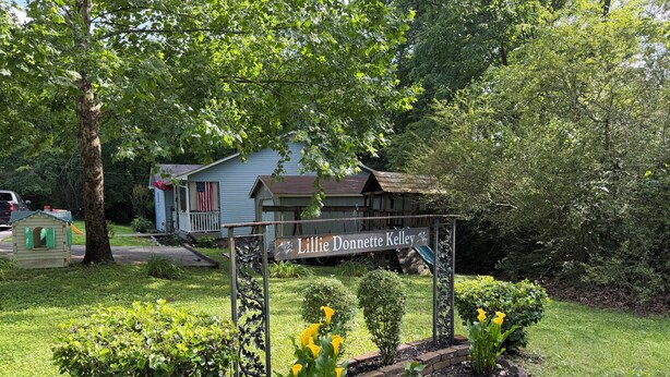 Un letrero con el nombre 'Lillie Donnett Kelley' en un jardín con una casa al fondo.