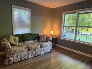 A room with a floral-patterned sofa, a lamp, and a window with a view of greenery.