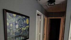 Un pasillo con un cuadro enmarcado en la pared, piso de madera y una puerta que da a otra habitación.