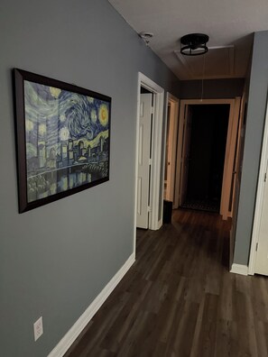 A hallway with a framed painting on the wall, wooden flooring, and a door leading to another room. - 3-bed/1-bath Home in charming Pegram - TriStar Tribe Country Cottage (Pegram)