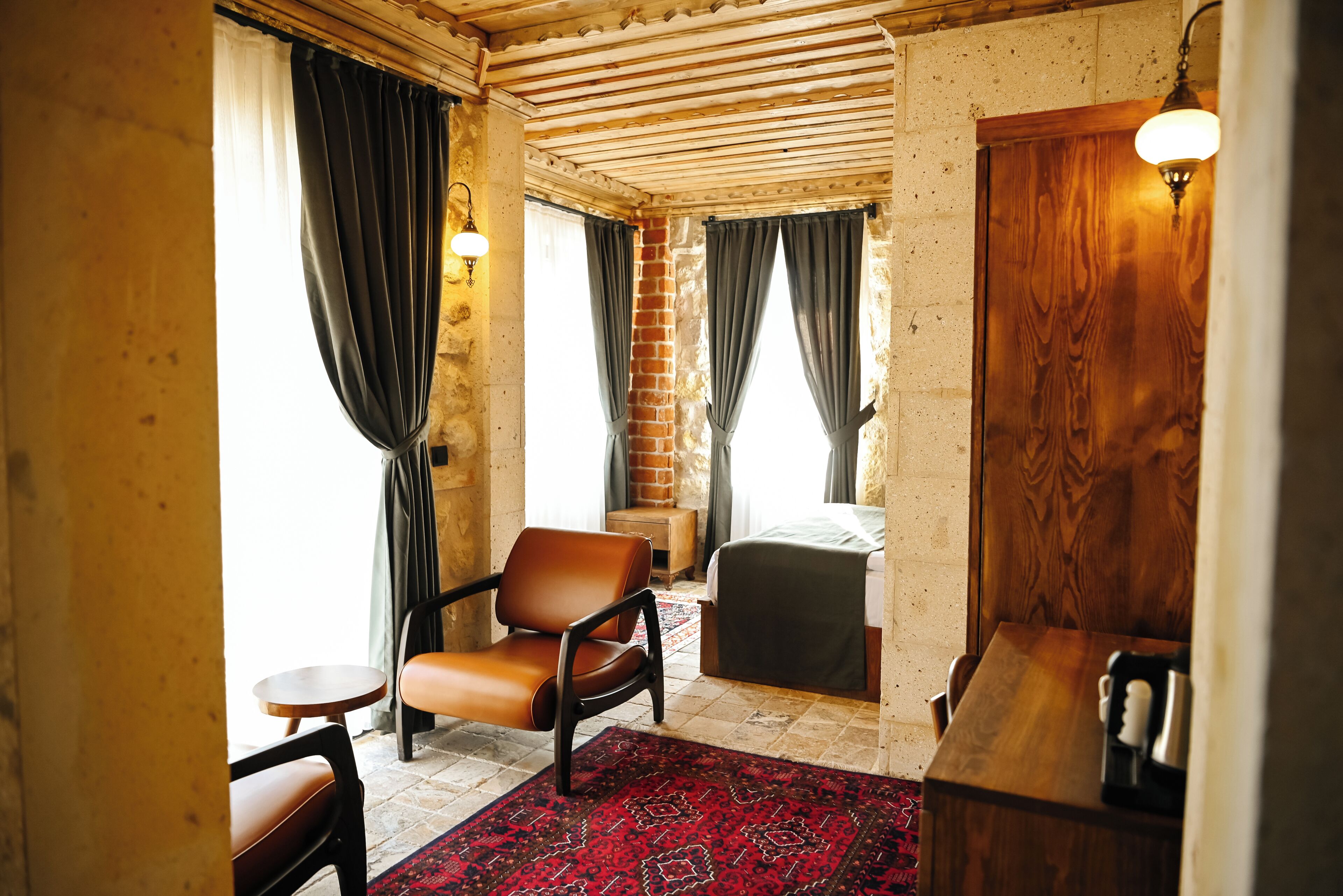 A room with a bed, a chair, a small table, a wooden bench, and a bar area with a coffee machine.