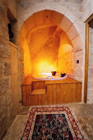 A stone-walled room with a wooden bench, a bathtub, and a patterned rug. - Honey of Cappadocia (Ürgüp)