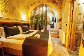 A hotel room with a bed, wooden headboard, and a view through an archway to a dining area. - Honey of Cappadocia (Ürgüp)