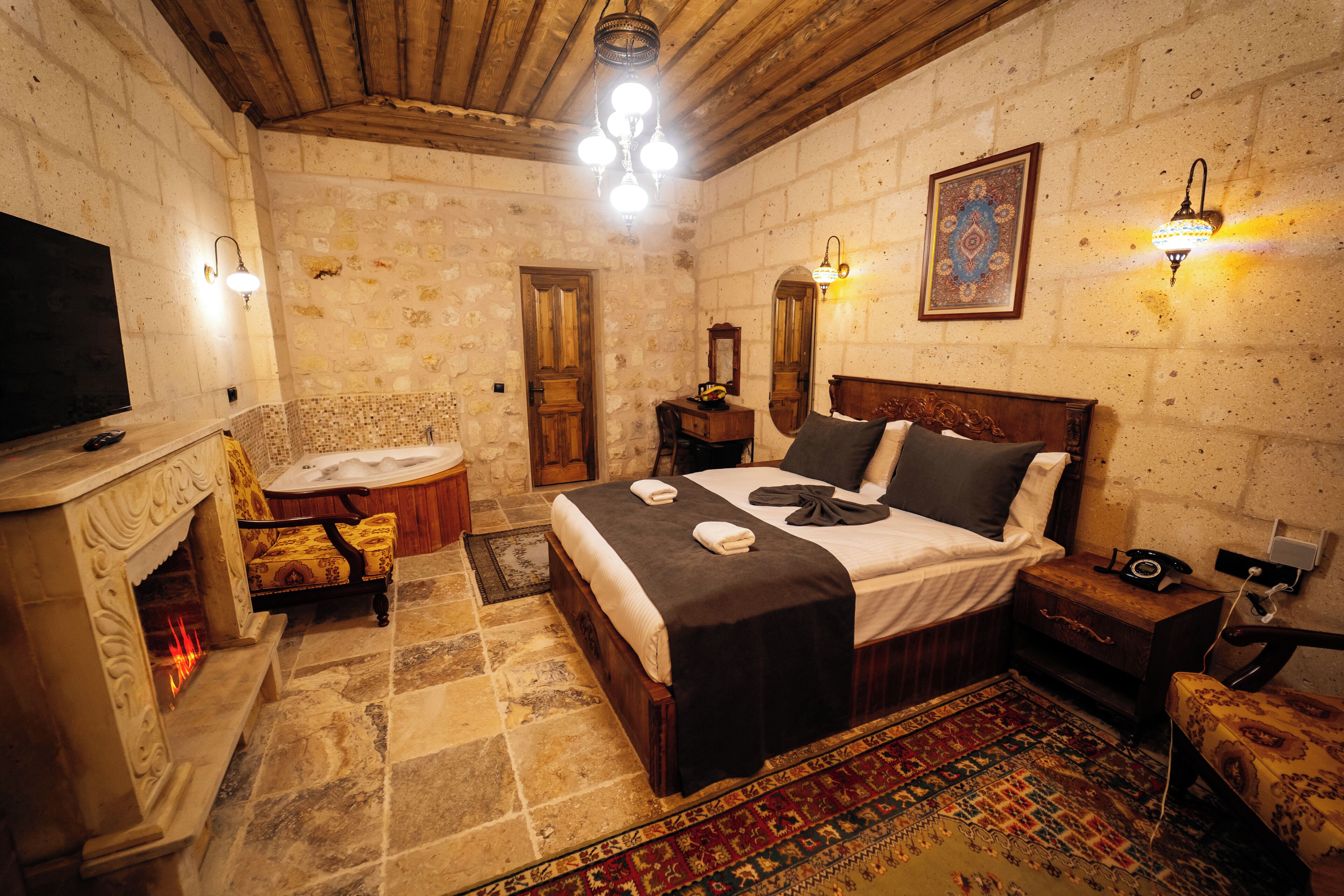 A room with a bed, a television, a fireplace, and a patterned rug.