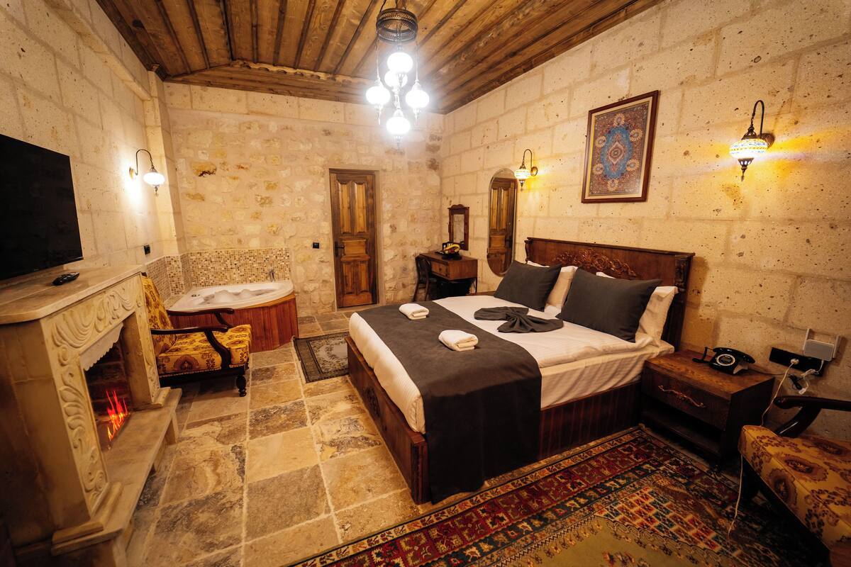 A room with a bed, a television, a fireplace, and a patterned rug.