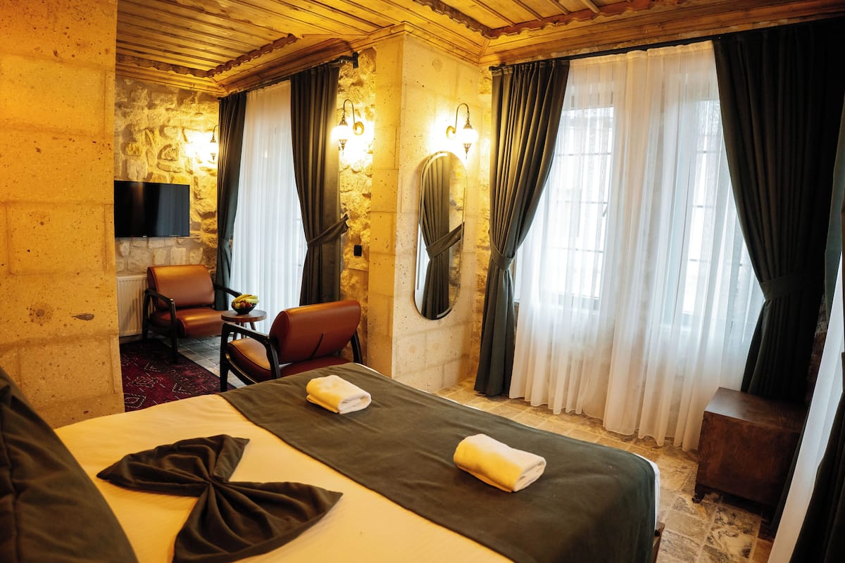 A hotel room with a bed, a chair, a TV, and a stone wall.