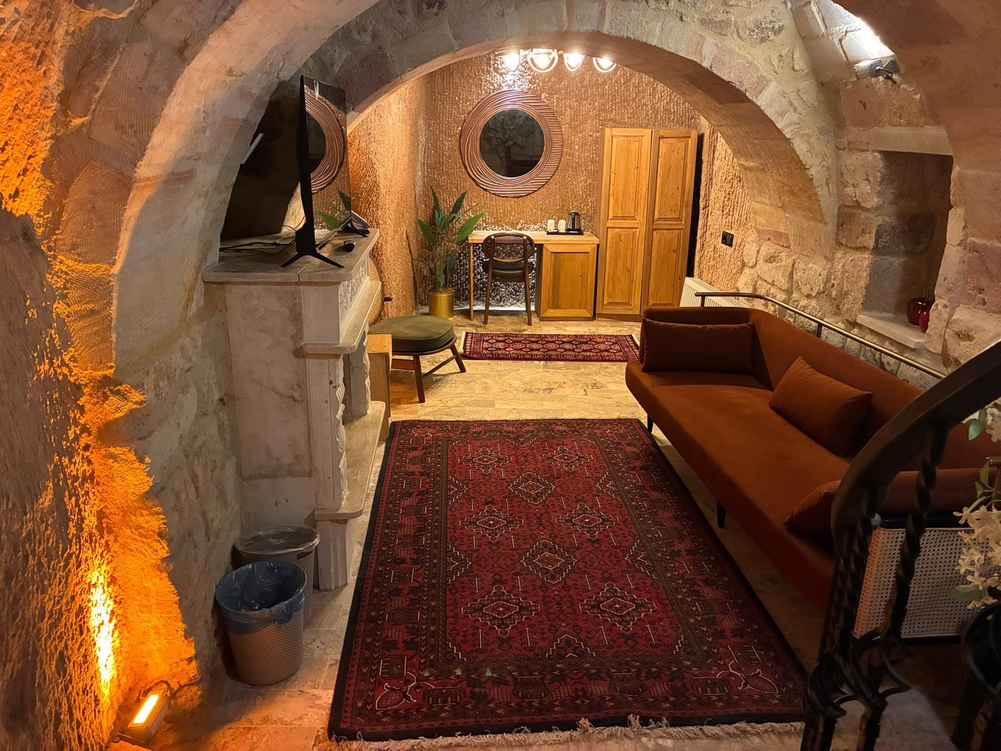 Interior con arco de piedra, un sofá, un tapete, una mesita y un armario de madera.