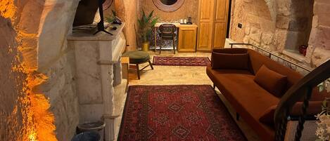 Interior con arco de piedra, un sofá, un tapete, una mesita y un armario de madera.