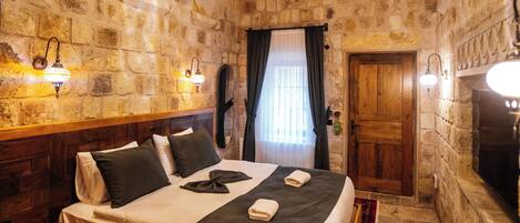 Una habitación de paredes de piedra con una cama, una mesa de madera con fruta y una chimenea.