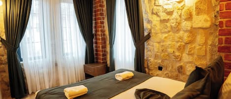 Una habitación de hotel con cama, cortinas, mesita de noche y pared de piedra.
