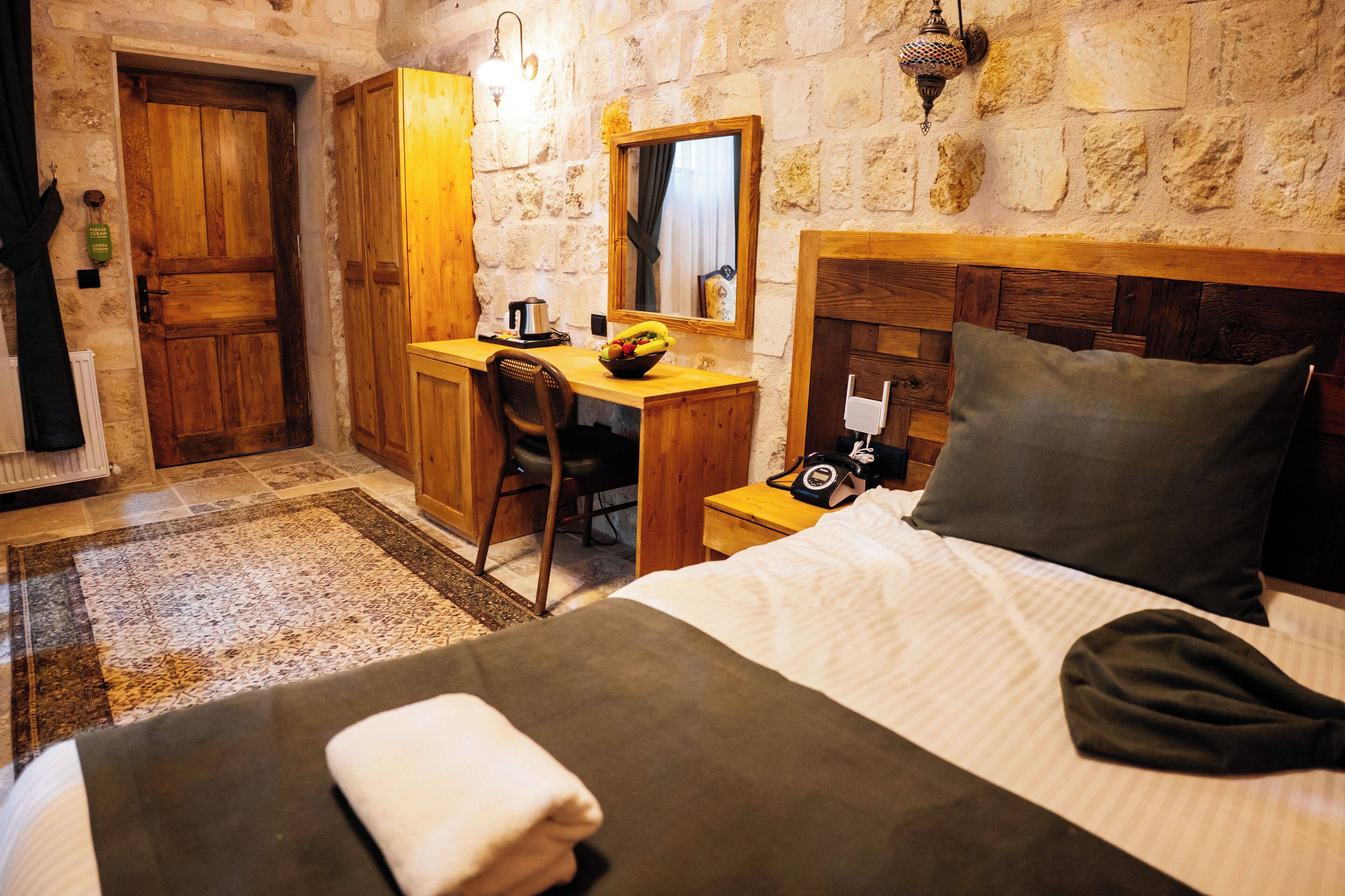 Une pièce comprenant un lit, un bureau, une chaise, une armoire en bois, un miroir et un mur en pierre.