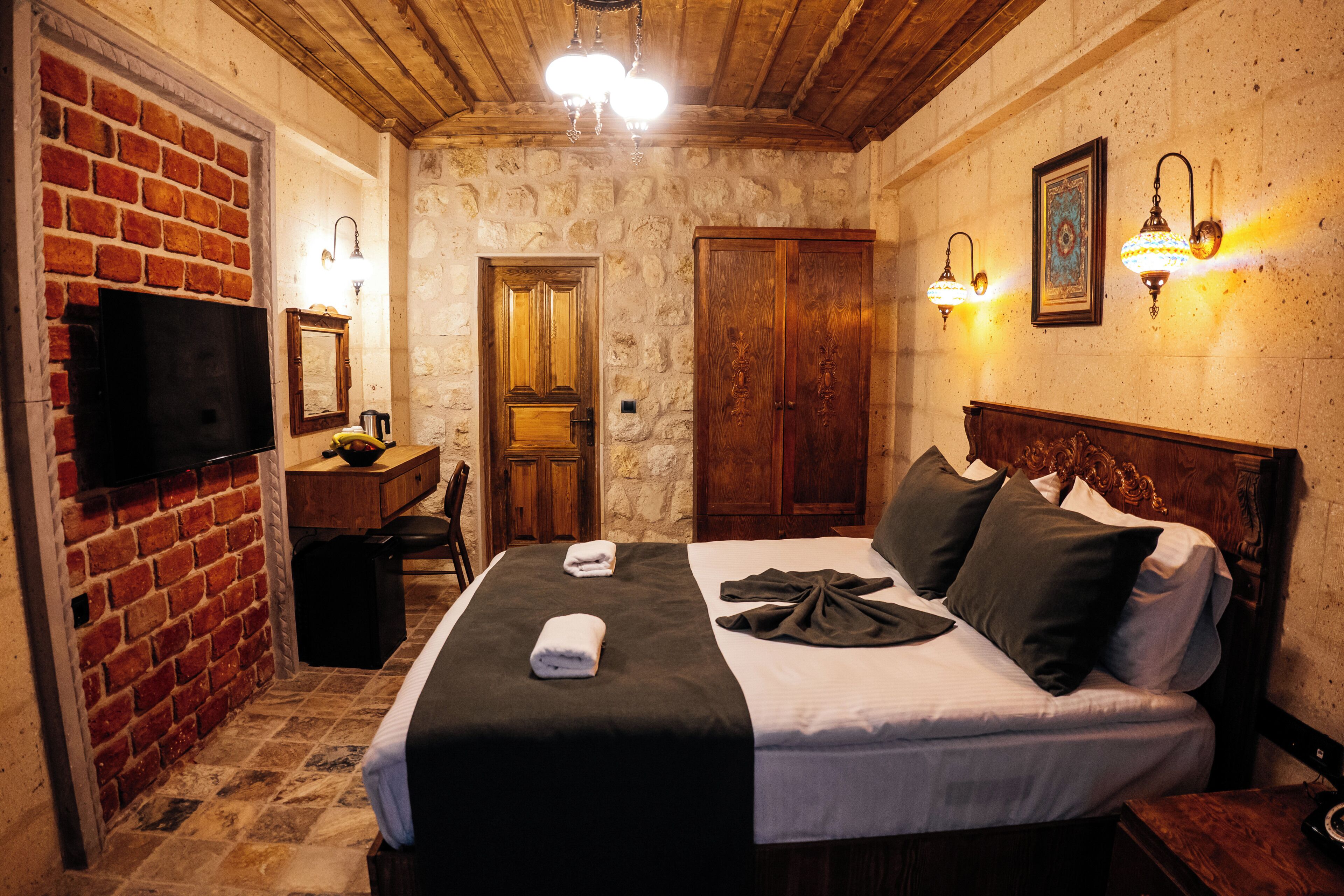 A hotel room with a brick fireplace, a bed with a black and white bedspread, a wooden headboard, and two wall-mounted lamps.