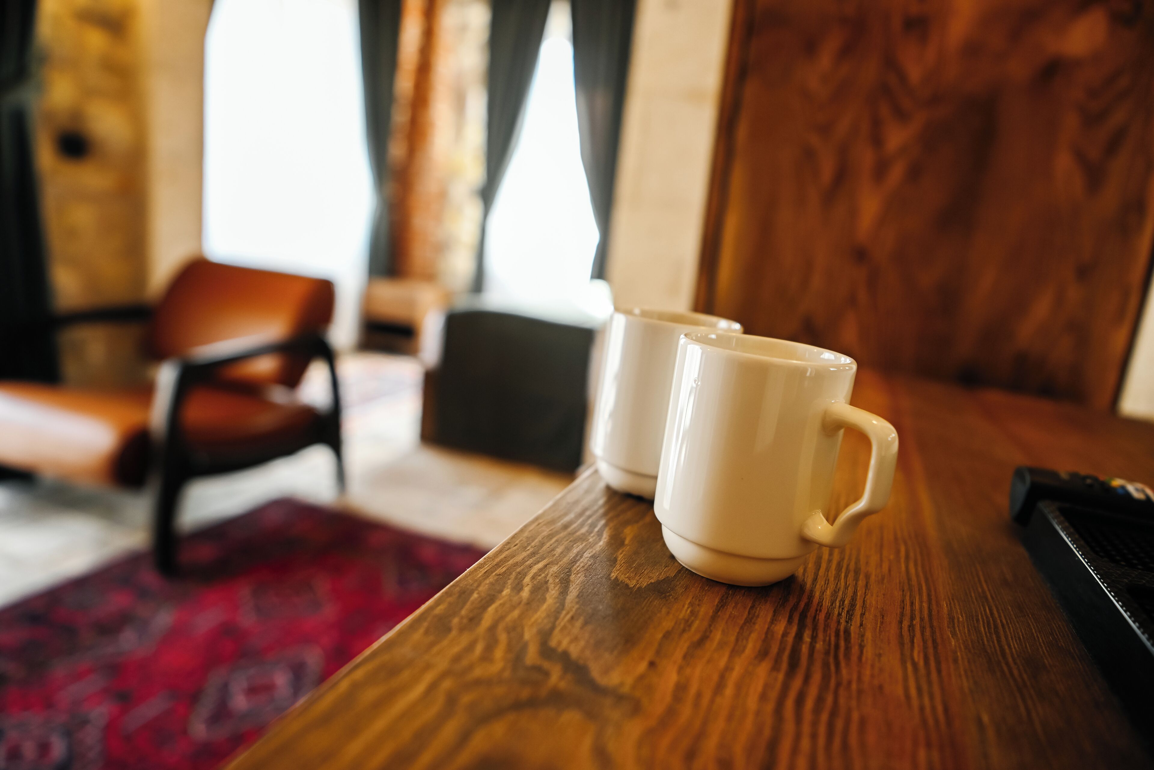 A wooden table with two white mugs, a brown chair, and a black object on the table.