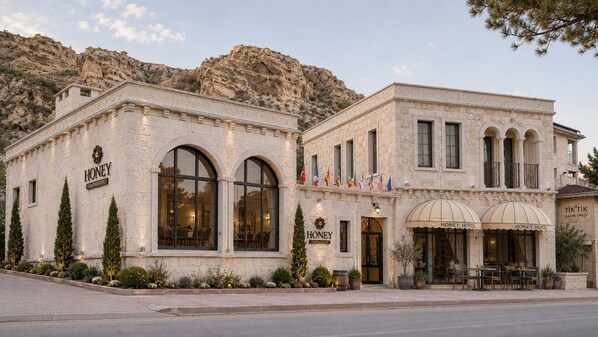 A hotel with arched windows, a stone facade, and a mountainous backdrop. - Honey of Cappadocia (Ürgüp)