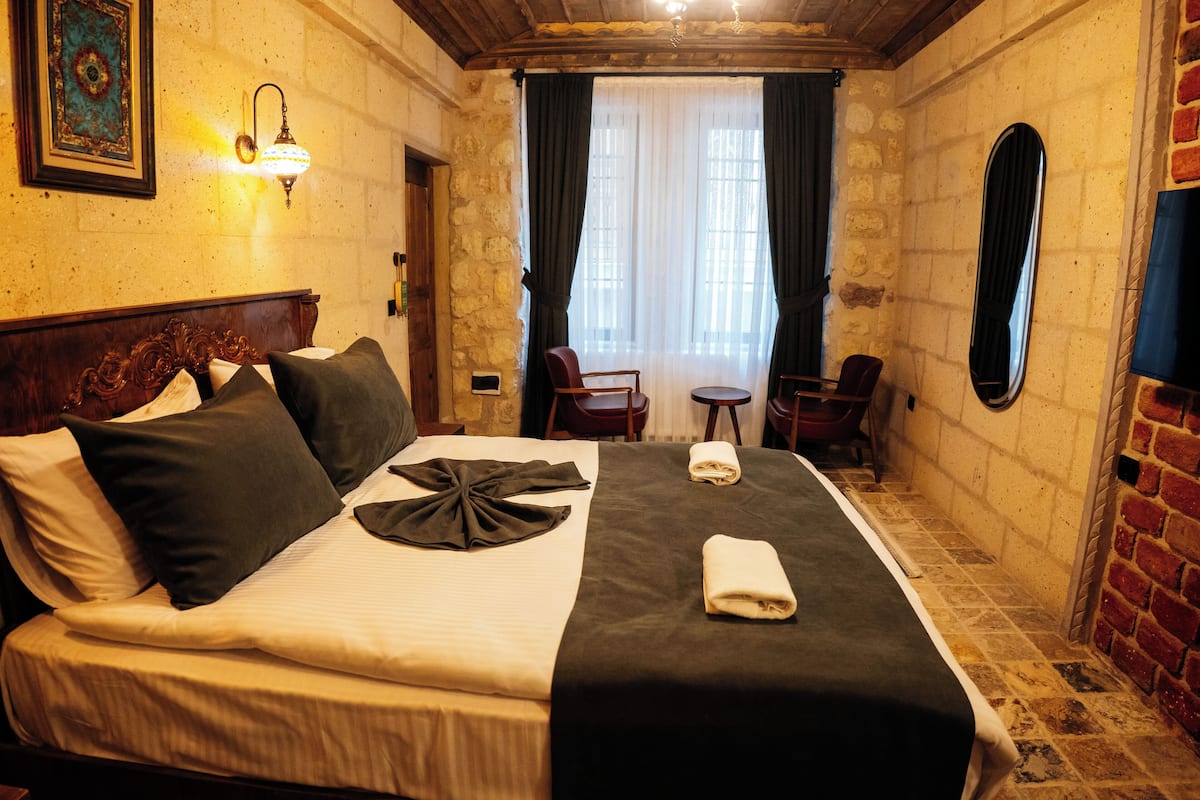 A hotel room with a bed, a small table, a chair, a mirror, and a wall-mounted lamp.
