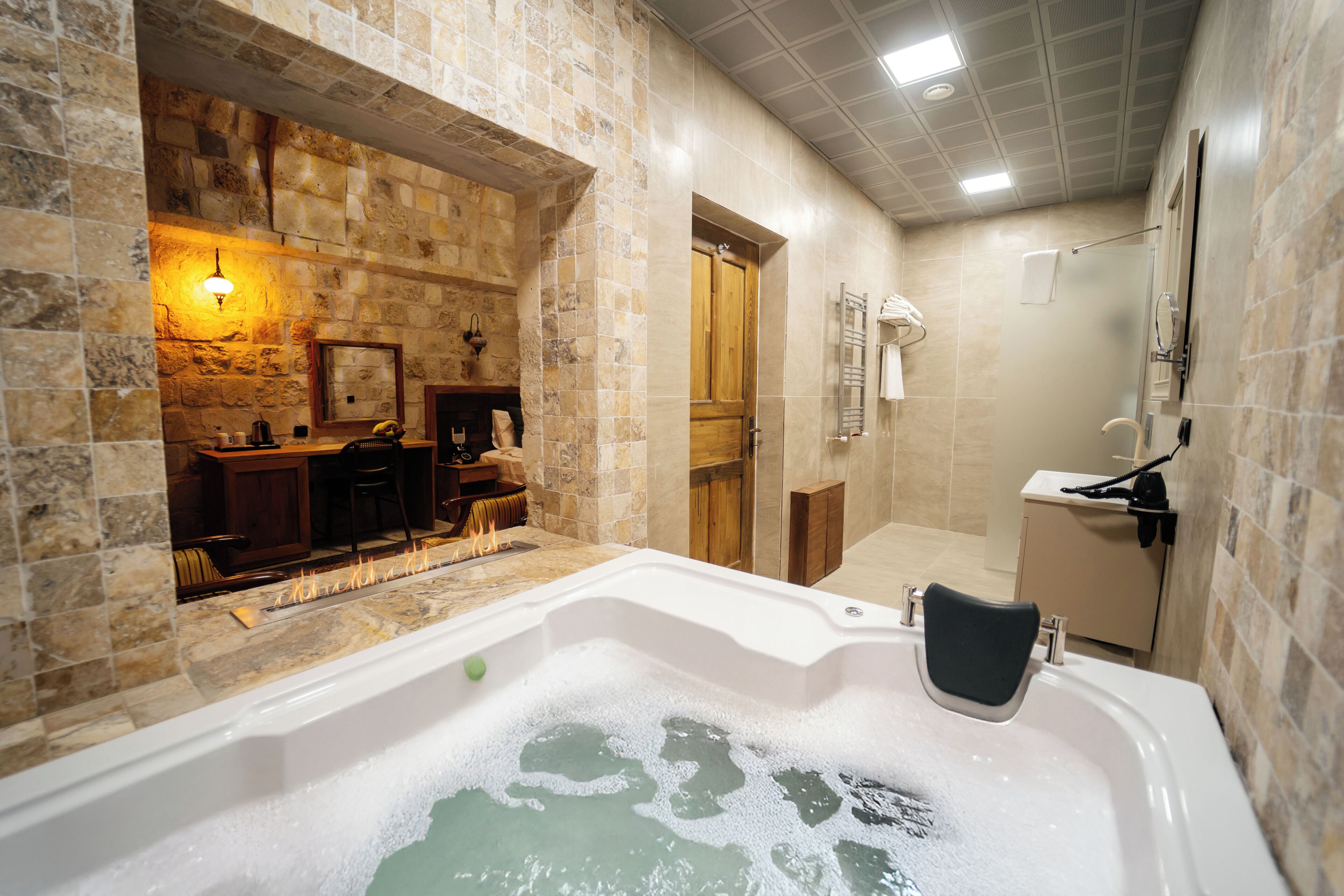 Un baño con pared de piedra, bañera, ducha y puerta de madera.
