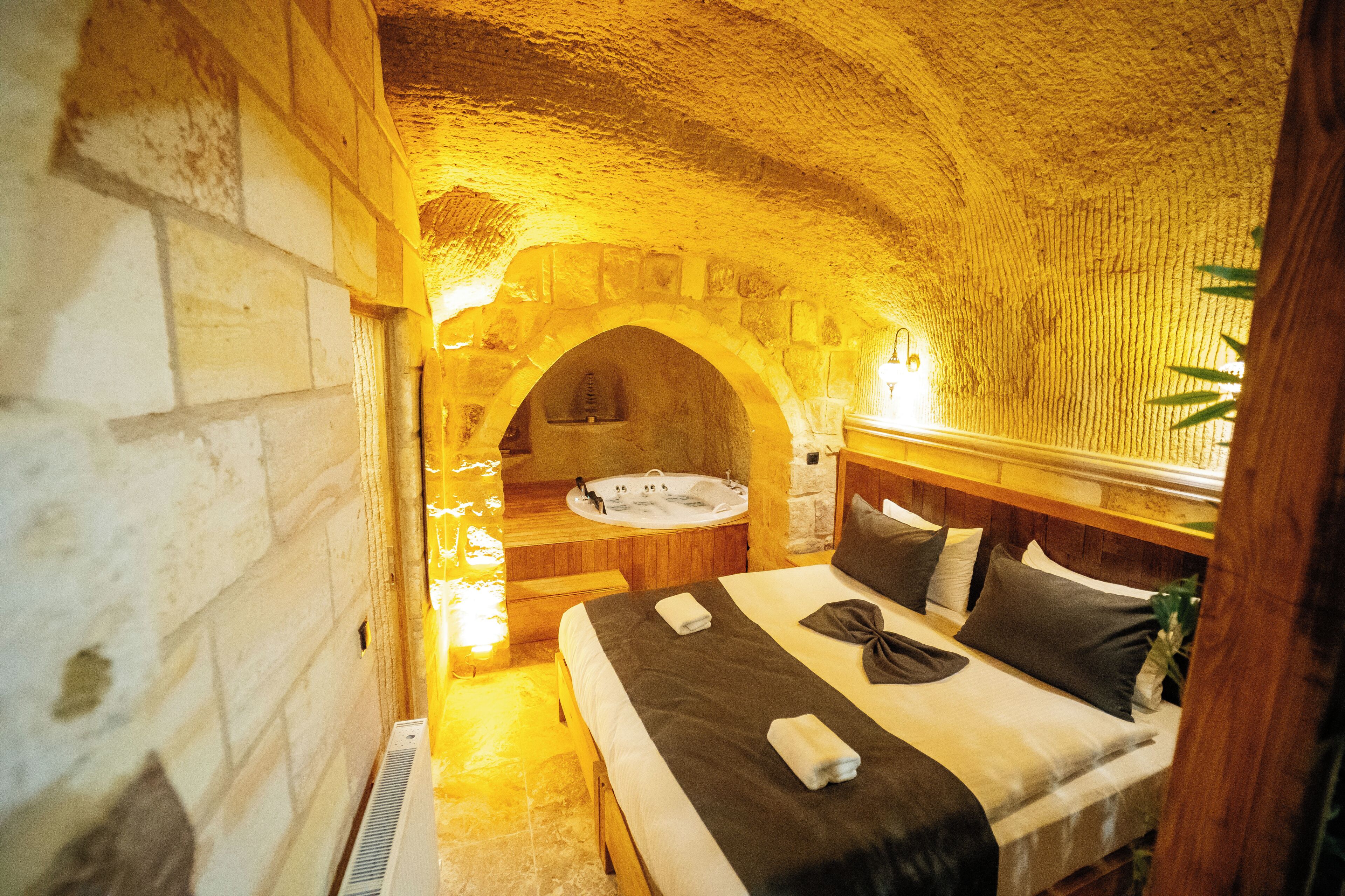 A room with a stone archway, a bed with a wooden headboard, a bathtub, and a wall-mounted heater.