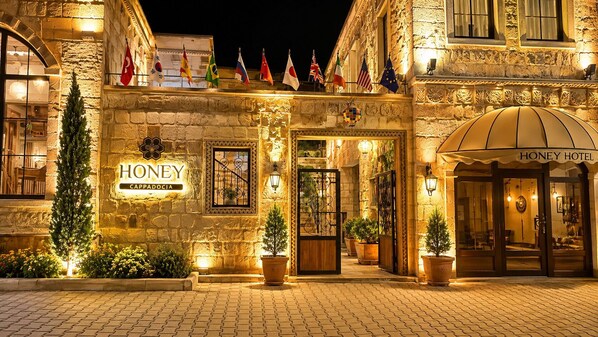 A hotel entrance with a sign reading 'HONEY CAPPADOCIA,' flags, and a well-lit facade.