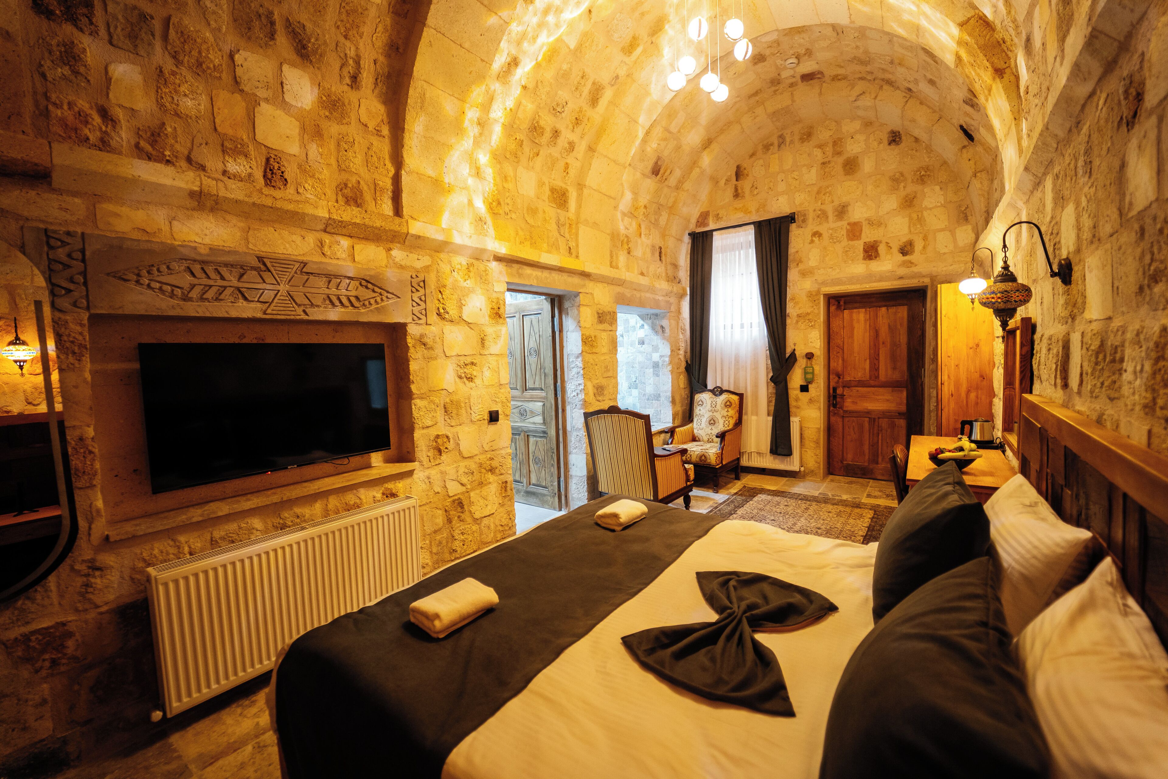 A stone-walled room with a bed, a television, a chair, and a table.