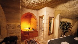 Ein Zimmer mit Steinwänden, einer hölzernen Bank, einem Bett und einem großen Spiegel.