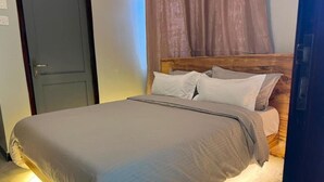 A neatly made bed with a wooden headboard, a closed door to the left, and a curtain partially drawn to the right. - Amala Homes – Private Stay in Mukono (Mukono)