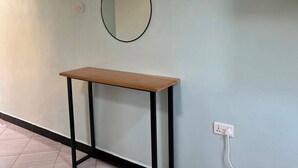 A room with a light blue wall, a round mirror, a wooden table with black legs, and a power outlet. - Amala Homes – Private Stay in Mukono (Mukono)