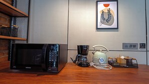 A kitchen with a microwave, coffee maker, and kettle on a wooden table.