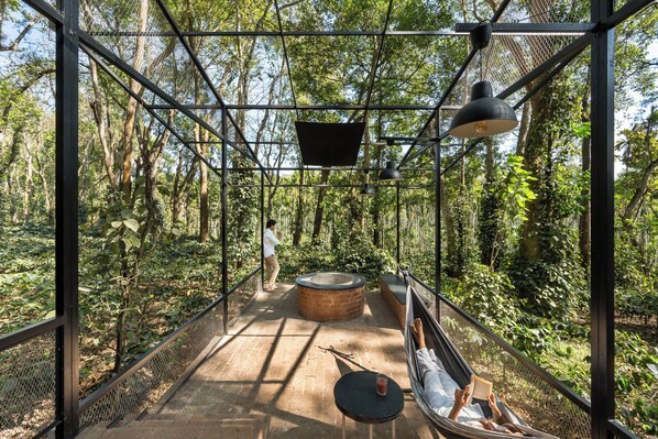 A hammock chair, a round brick fire pit, and a metal mesh structure in a forested area.