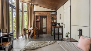 A modern room with a bed, desk, and dining area, featuring large windows and a brick wall. - Container cabin retreat on a 70-acre Coorg estate with estate views (Siddapur)