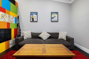 A modern living room with a grey sofa, two framed posters, a wooden coffee table, and a colorful abstract painting on the wall.