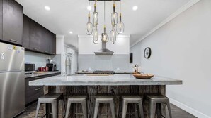 Uma cozinha moderna com uma ilha grande, banquetas e um lustre pendente.