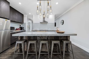 A modern kitchen with a large island, bar stools, and a hanging light fixture.