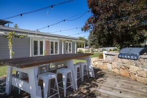 A wooden deck with a bar table and stools, a grill, and a house in the background. - Edelweiss Cottage - Serene and spacious Berridale Accommodation (Berridale)