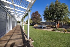 A covered patio with a wooden deck, a white pergola, a small outdoor seating area, and a well-maintained lawn. - Edelweiss Cottage - Serene and spacious Berridale Accommodation (Berridale)