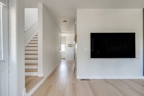 A hallway with a staircase, a flat-screen TV mounted on the wall, and a door on the left. - Modern Home Near Old Mill & River (Bend)
