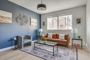 A modern living room with a blue accent wall, a sofa, a coffee table, and a window with a view. - Modern Home Near Old Mill & River (Bend)