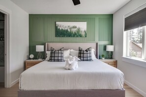 A bedroom with a bed, two bedside tables, a nightstand, a wall-mounted painting, and a window with blinds. - Modern Home Near Old Mill & River (Bend)