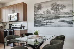A modern kitchen with wooden cabinets, a microwave, and a dining area with a glass table and four chairs. - Modern Home Near Old Mill & River (Bend)